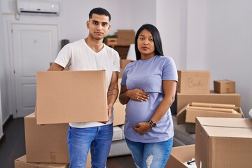 Fototapeta na wymiar Young hispanic couple expecting a baby moving to a new home relaxed with serious expression on face. simple and natural looking at the camera.