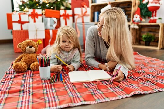 Mother and daughter drawing on notebook lying by christmas tree at home