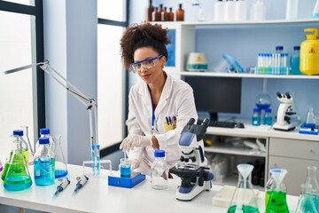 Young african american woman wearing scientist uniform measuring liquid at laboratory