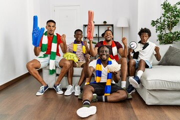Young african men wearing team scarf cheering football game screaming proud, celebrating victory...
