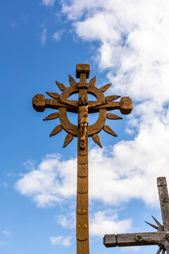 Vertical photo big light brown wooden cross – handmade carpentry art at hill of crosses near Šiauliai, Lithuania. Great ornamental timber Catholic cross with crucified Jesus against cloudy sky 