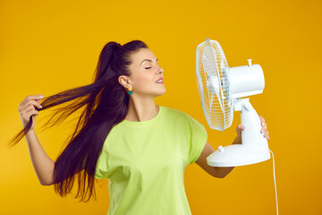 Woman enjoys fresh air and escapes summer heat with electric fan isolated on orange background....