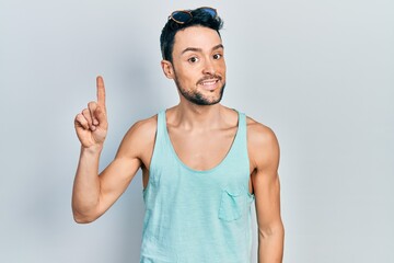 Young hispanic man wearing summer style smiling with an idea or question pointing finger up with...