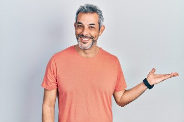 Handsome middle age man with grey hair wearing casual t shirt smiling cheerful presenting and pointing with palm of hand looking at the camera.