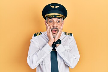 Handsome middle age man with grey hair wearing airplane pilot uniform afraid and shocked, surprise...