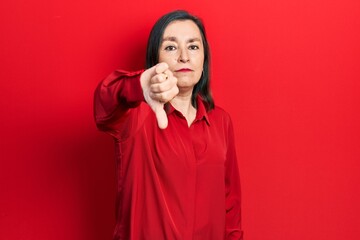 Middle age hispanic woman wearing casual clothes looking unhappy and angry showing rejection and negative with thumbs down gesture. bad expression.