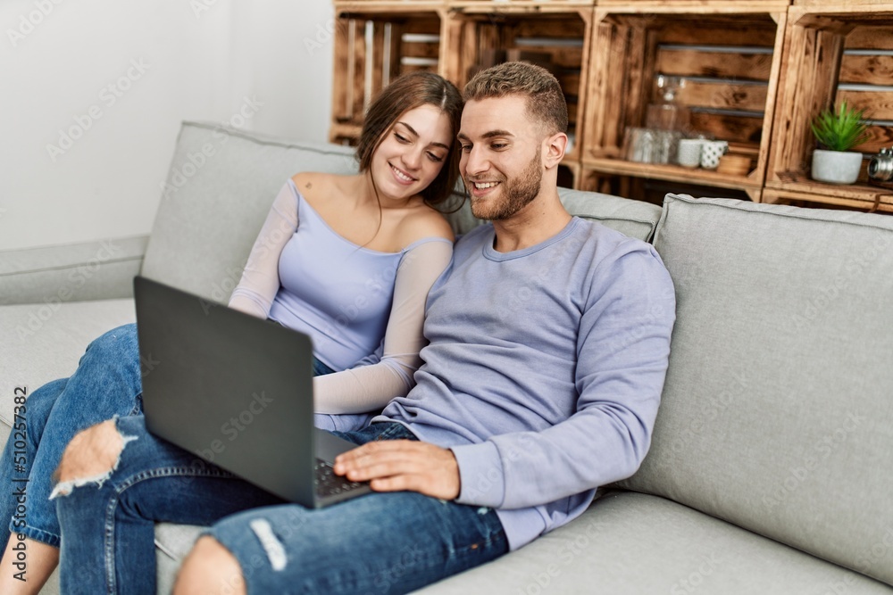 Sticker Young caucasian couple using laptop sitting on the sofa at home.