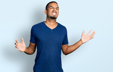 Young african american man wearing casual t shirt crazy and mad shouting and yelling with aggressive expression and arms raised. frustration concept.