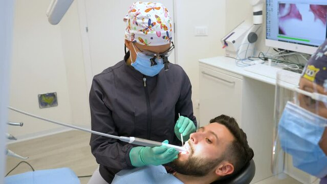 Female dentist examines a man patient in a dental office using professional tools and personal protective equipment.