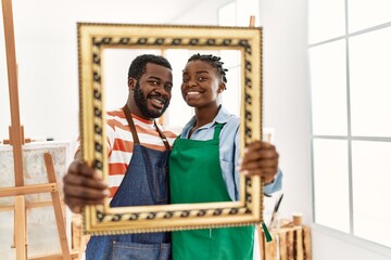African american painter couple smiling happy holding empty frame at art studio.