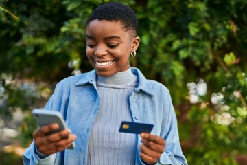 Young african american woman smiling happy holding smartphone and credit card at the city