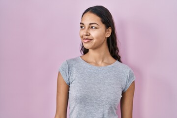 Young brazilian woman wearing casual t shirt over pink background smiling looking to the side and staring away thinking.