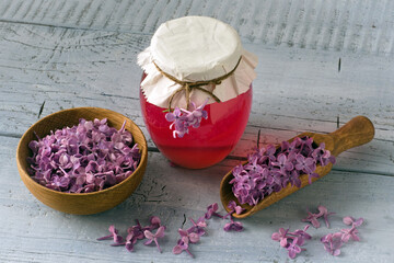 Lilac flowers syrup in glass jar and lilac flower petals on wooden background.