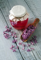 Healthy lilac flowers syrup in glass jar and lilac flower petals on wooden background.