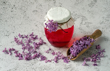 Lilac flowers syrup in glass jar and lilac blossoms on grey background.