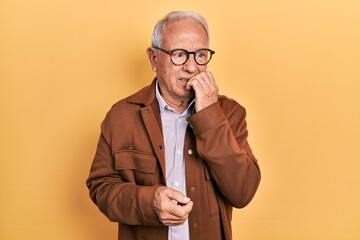 Senior man with grey hair wearing casual jacket and glasses looking stressed and nervous with hands on mouth biting nails. anxiety problem.