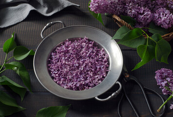 Lilac buds and petals in a vintage metal bowl on dark wooden table.