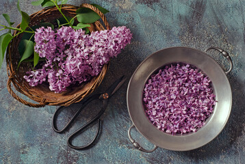 Lilac buds and petals in a vintage metal bowl and basket on textured background. Top view.