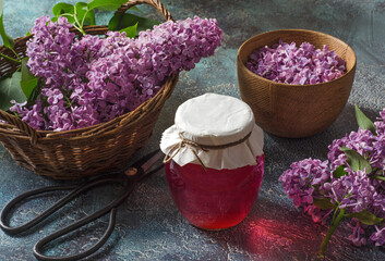 Lilac flowers syrup in glass jar and lilac buds on textured background.