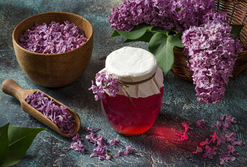 Healthy lilac flowers syrup in glass jar and lilac flower petals on textured background.