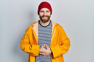 Caucasian man with beard wearing yellow raincoat smiling and laughing hard out loud because funny crazy joke with hands on body.