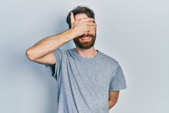 Caucasian man with beard wearing casual grey t shirt smiling and laughing with hand on face covering eyes for surprise. blind concept.
