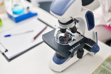 Young hispanic woman wearing scientist uniform using microscope at laboratory