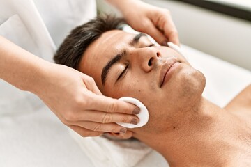 Fototapeta na wymiar Young hispanic man relaxed having facial treatment cleaning face with cotton disk at beauty center