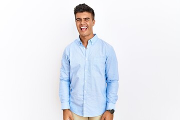 Fototapeta premium Young hispanic man wearing business shirt standing over isolated background winking looking at the camera with sexy expression, cheerful and happy face.