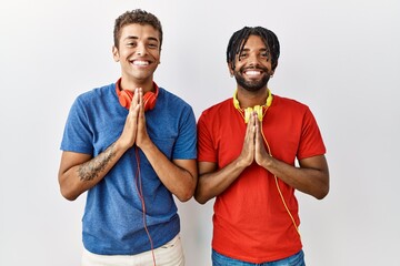 Young hispanic brothers standing over isolated background wearing headphones praying with hands...