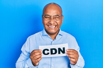 Middle age latin man holding cdn message paper winking looking at the camera with sexy expression, cheerful and happy face.