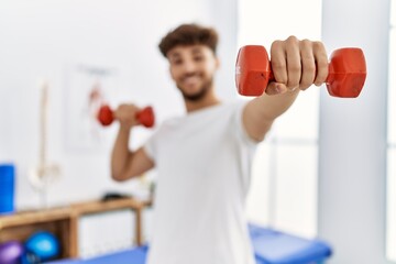 Young arab man patient doing rehab using dummbells at clinic