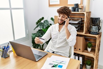 Young arab man talking on the smartphone and holding credit card working at office