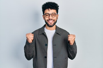Young arab man with beard wearing glasses celebrating surprised and amazed for success with arms...