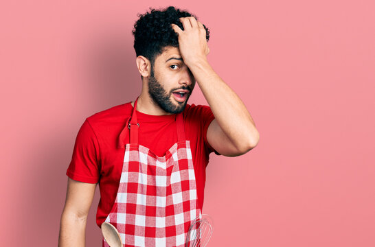 Young Arab Man With Beard Wearing Cook Apron Surprised With Hand On Head For Mistake, Remember Error. Forgot, Bad Memory Concept.