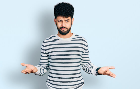 Young arab man with beard wearing casual striped sweater clueless and confused with open arms, no idea concept.