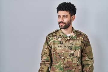 Arab man wearing camouflage army uniform smiling looking to the side and staring away thinking.