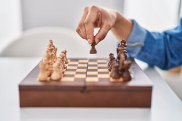 Young arab man playing chess sitting on table at home