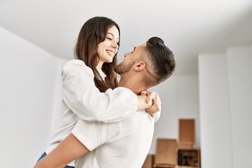 Fototapeta premium Young hispanic man holding woman in arms and hugging at new home.