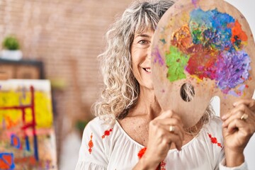 Middle age woman holding painter palette covering face smiling with a happy and cool smile on face....