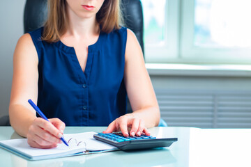 Woman accountant with calculator. Business expenses audit concept. Calculator is on girl desk. Businesswoman considers income of company. Girl is using calculator. Entrepreneur woman making notes