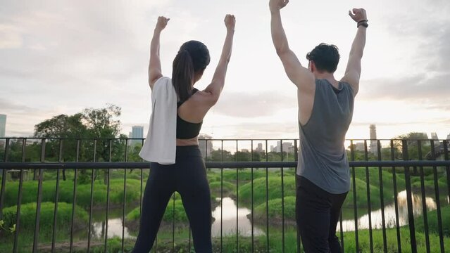 Asian fitness couple celebrating their achievement after success with intense workout training program at park, screaming with raised hands, reaching the finish line or goals, fitness partnership.
