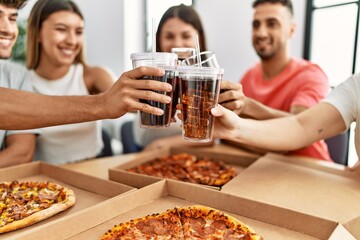 Group of young friends smiling happy eating italian pizza and toasting with cola beverage at home.
