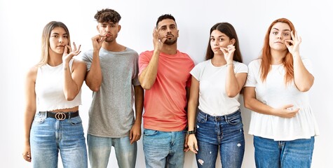 Obraz premium Group of young friends standing together over isolated background mouth and lips shut as zip with fingers. secret and silent, taboo talking