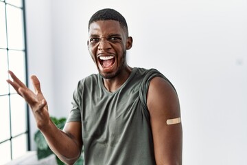 Young african american man getting vaccine showing arm with band aid celebrating victory with happy...