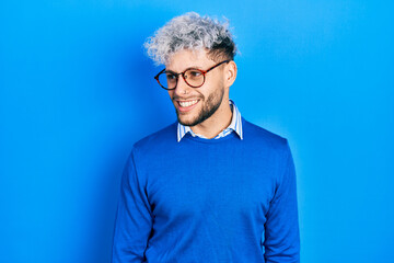 Young hispanic man with modern dyed hair wearing sweater and glasses looking away to side with smile on face, natural expression. laughing confident.