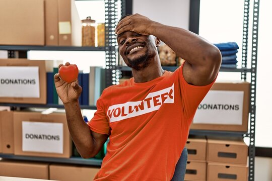 Young african man wearing volunteer t shirt at donations stand holding heart stressed and frustrated with hand on head, surprised and angry face