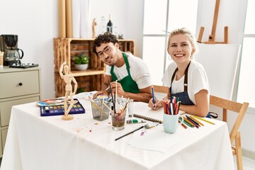 Young artist couple smiling happy painting at art studio.