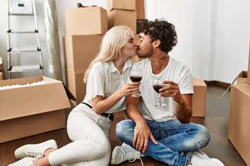Young beautiful couple kissing and toasting with red wine at new home