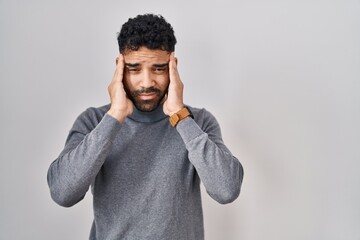 Hispanic man with beard standing over white background with hand on head, headache because stress....